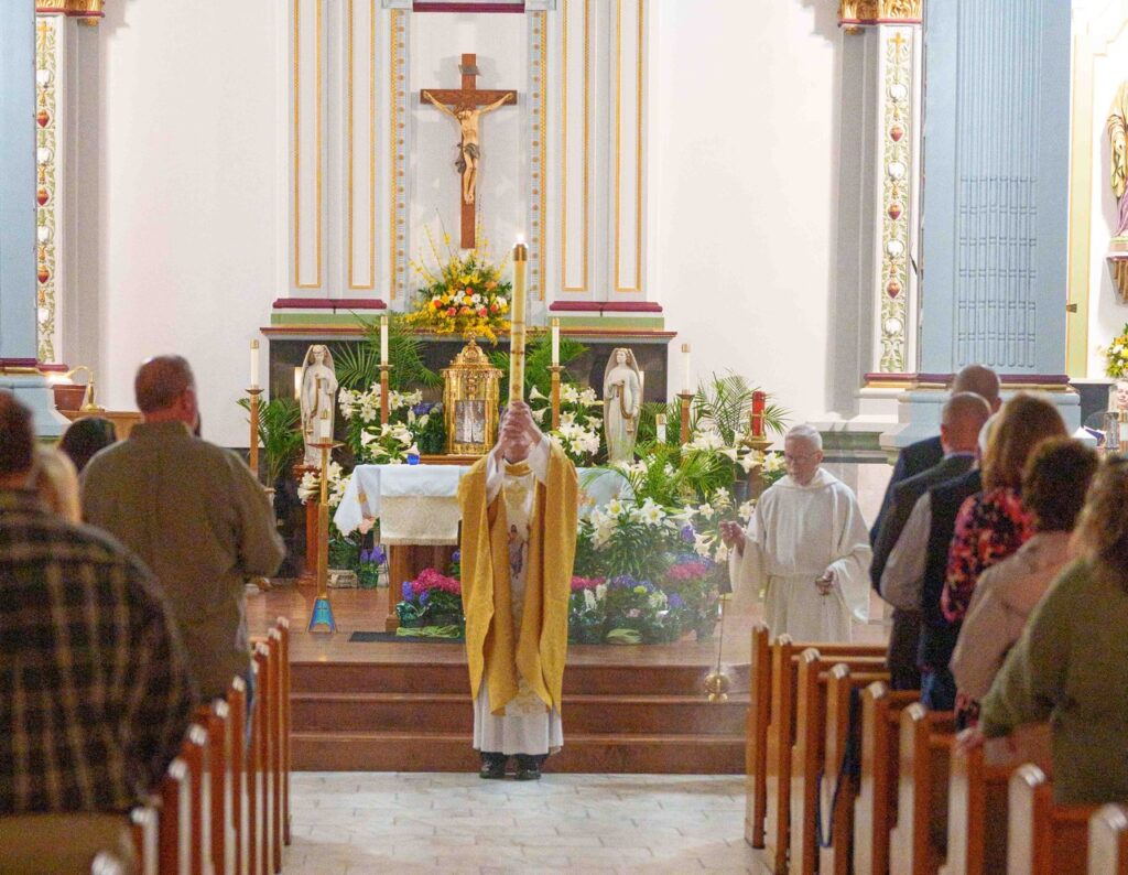 Priest raises the Easter candle in front of the altar at the Easter Vigil 2024 at Holy Trinity Parish in East Liverepool. Photo by Jimmy Joe Savage.