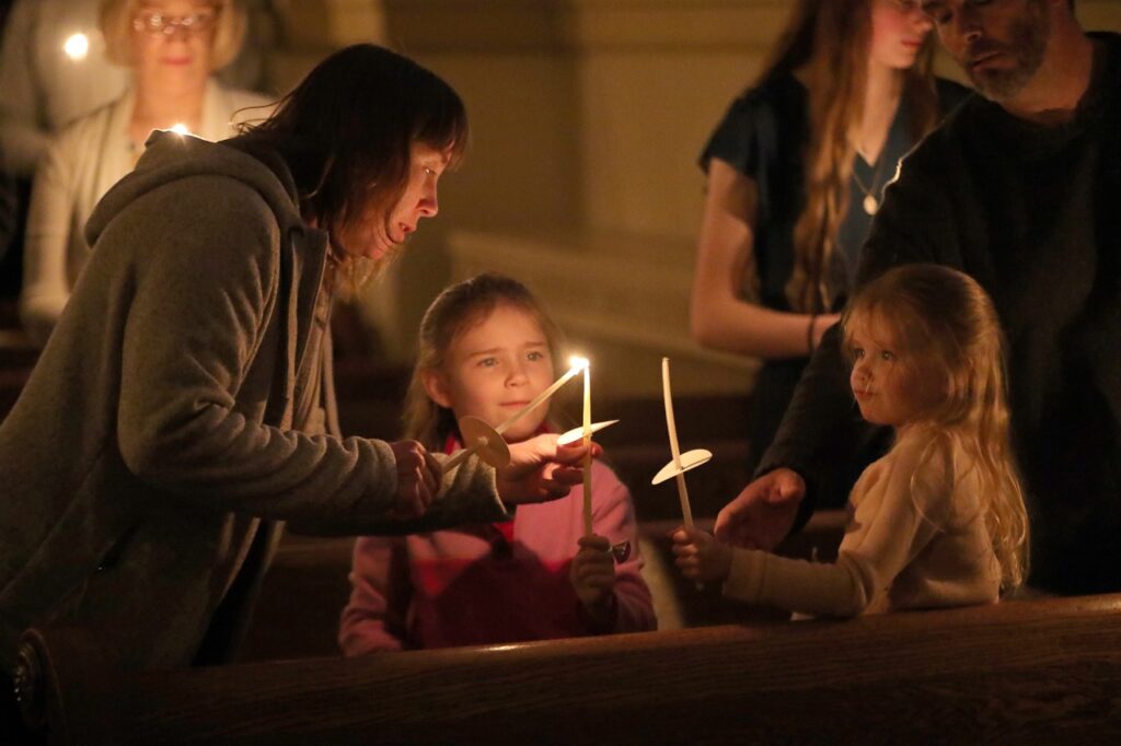 Mother lights daughters' candles at St. Joseph Parish in Mogadore during the Easter Vigil 2024. Photo by Ed Hall, Jr.