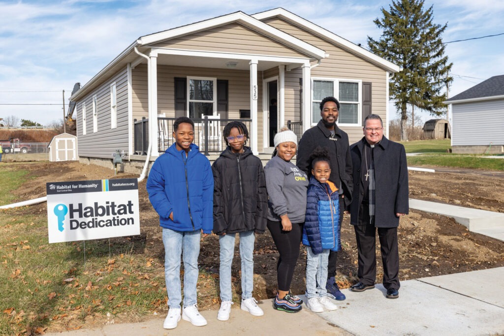 The Mathis family poses with bishop Bonnar in front of their new home.