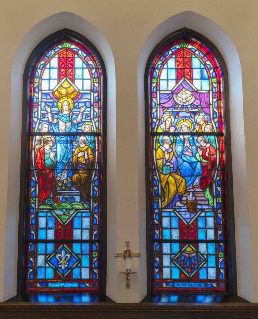 Two Stained Glass windows. On the left, Mary stands with hands raised during her assumption. On the right, a dove shines light on people below. Located at Immaculate Conception Parish in Ravenna. Photo by Brian Keith.