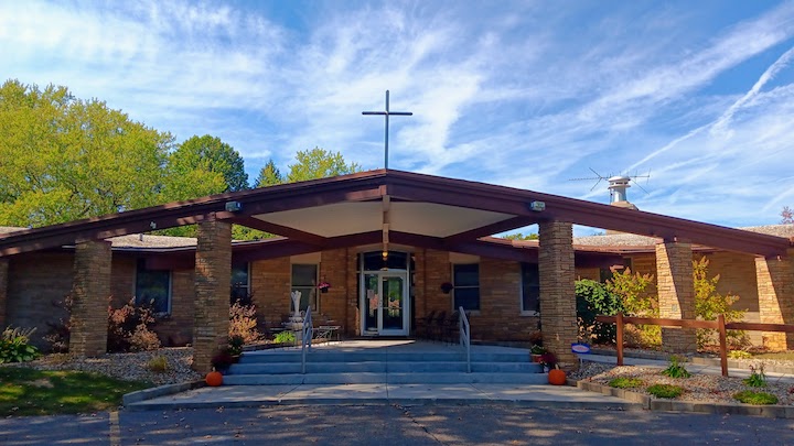 Image of wide, a-frame style building surrounded by trees.