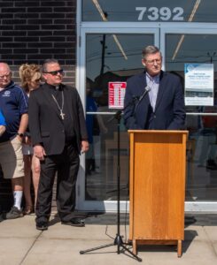 bishop bonnar watches man speaking at a podium at St. vincent de paul thrift store. photo by courtney poullas