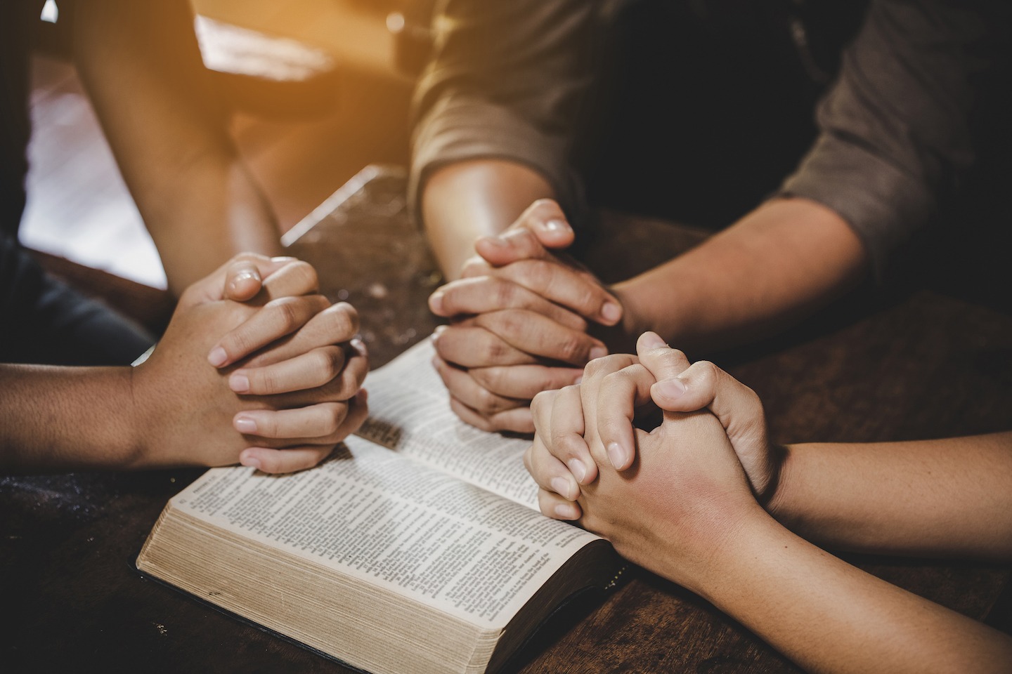 Stock photo of people praying together around a bible