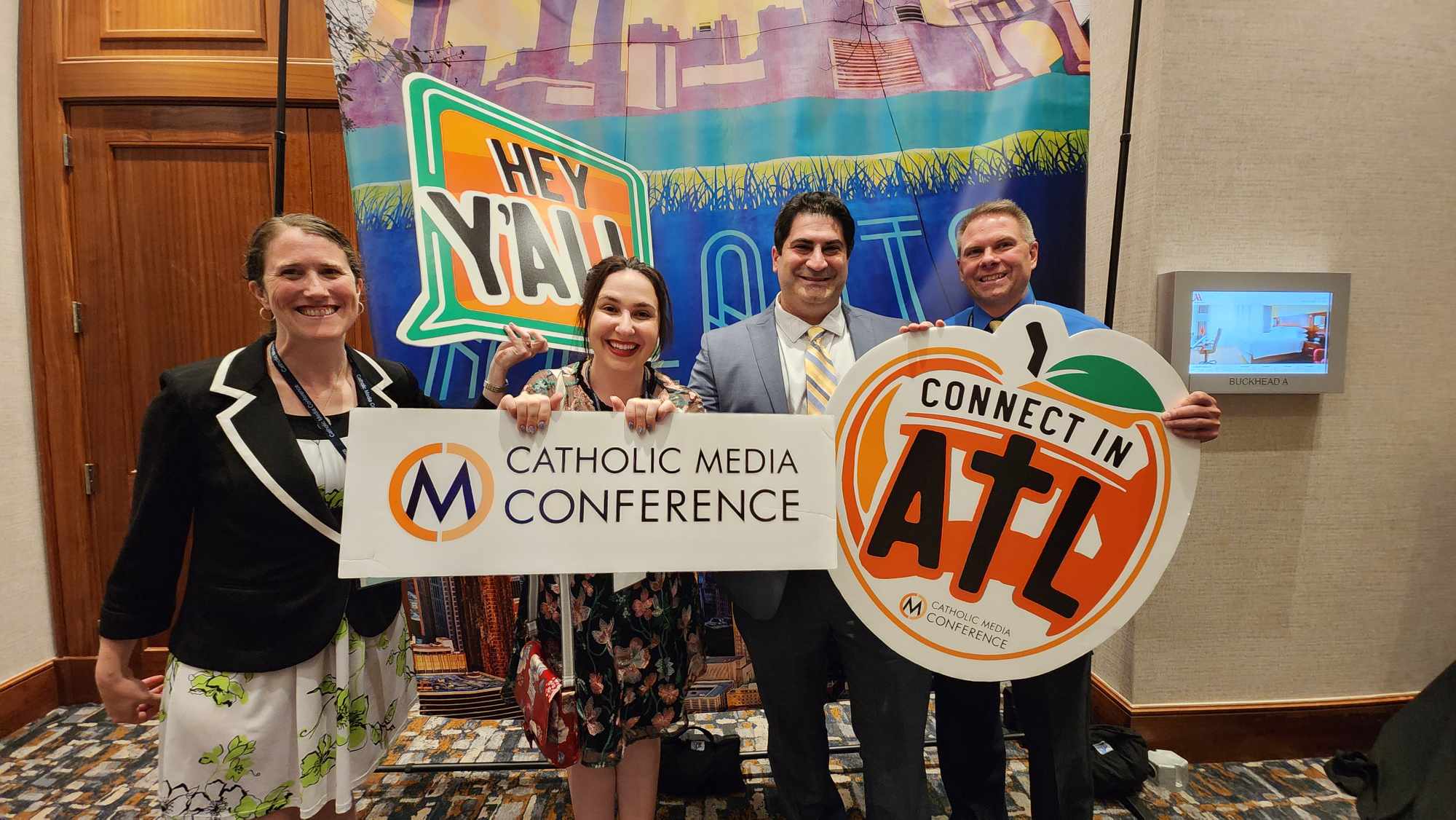 Four people stand in front of a step-and-repeat, holding props from the conference in Atlanta