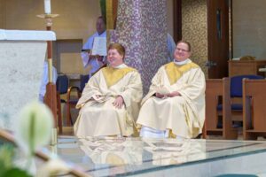 Two new priests smile, seated, during their ordination Mass