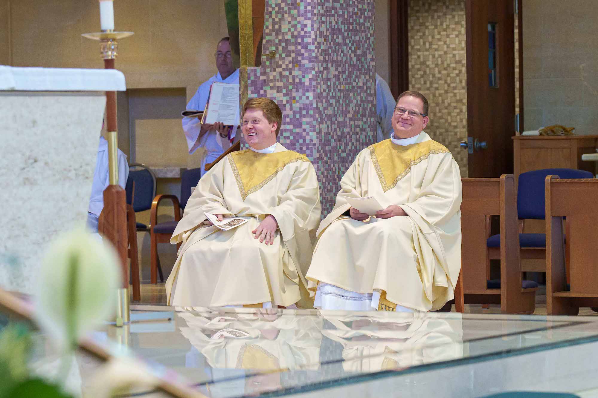 Two new priests smile, seated, during their ordination Mass