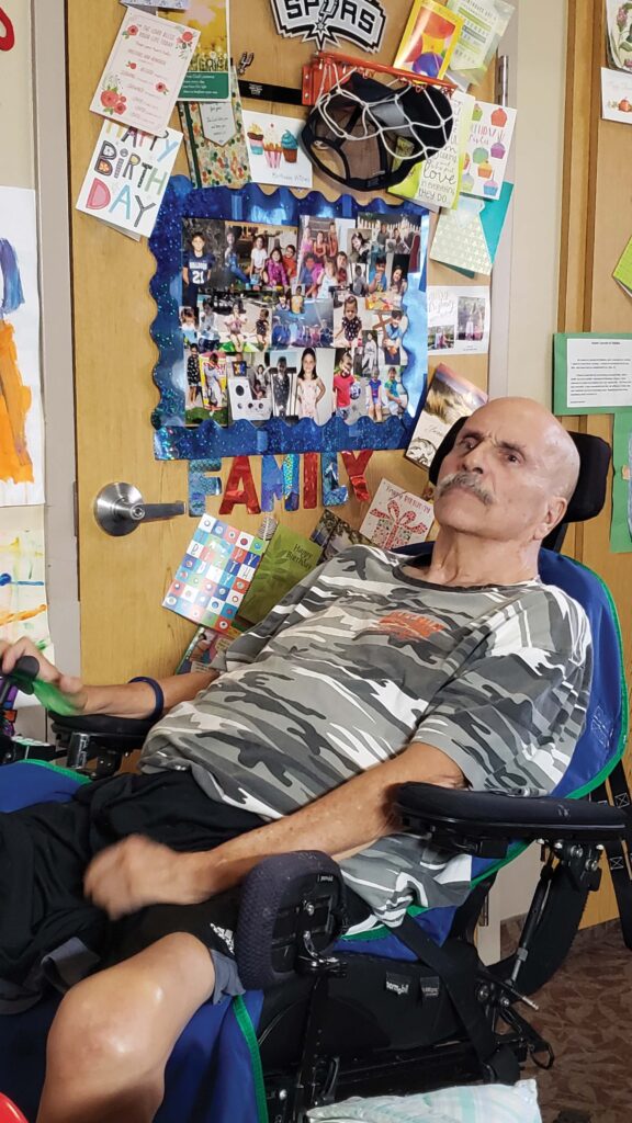 Image of Father Popovich in a wheelchair in his home