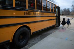 Two kids hold hands as they walk off a school bus