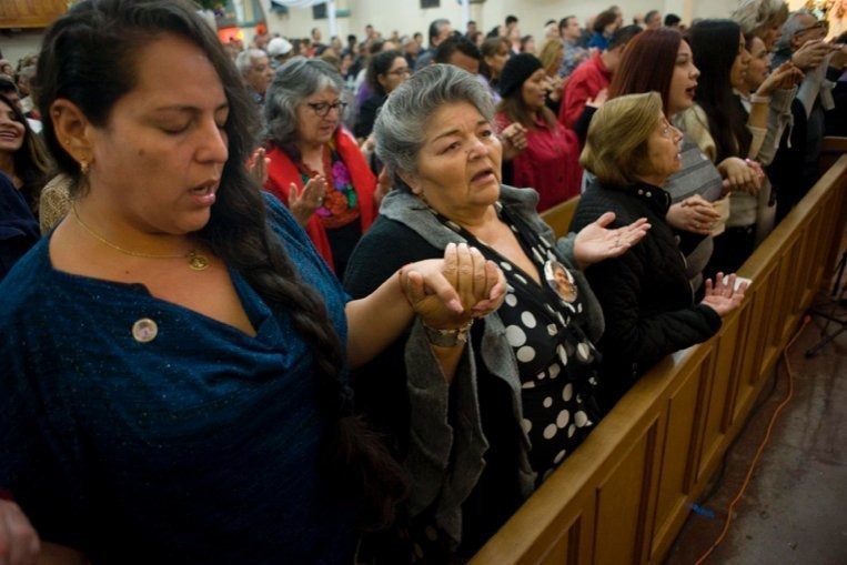 For latina women clasp hands in prayer during Mass