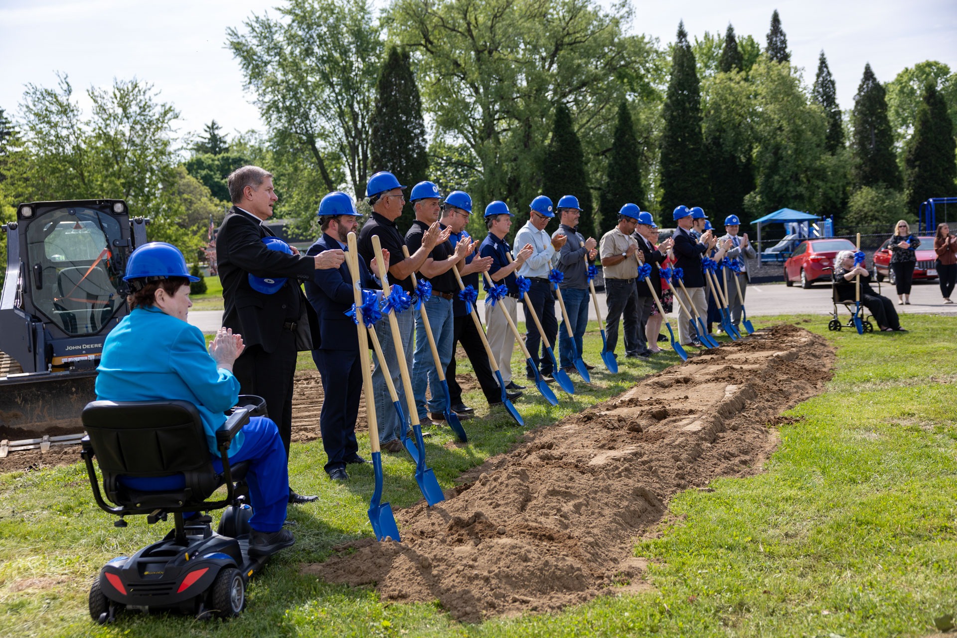 Dozens of people, including Monsignor Zuraw, line up with blue shovels to break ground on the new building.