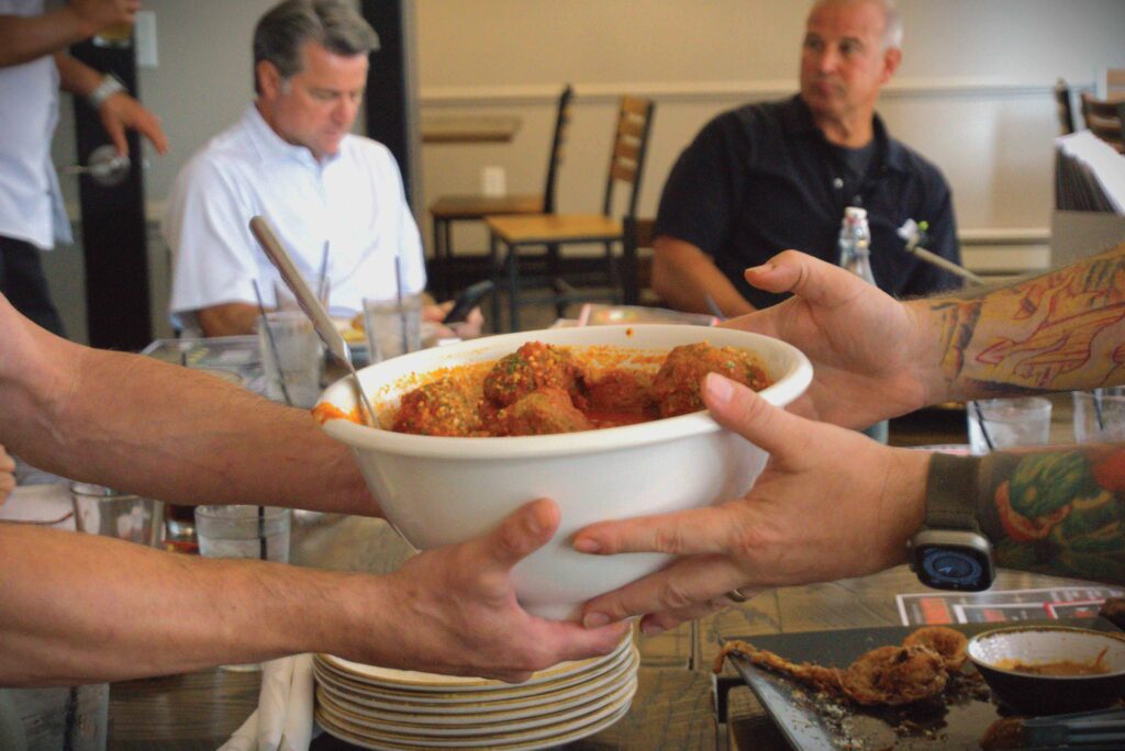 Two hands grabbing a bowl of meatballs