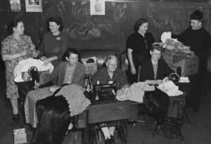 Several women, sitting and standing around sewing machines