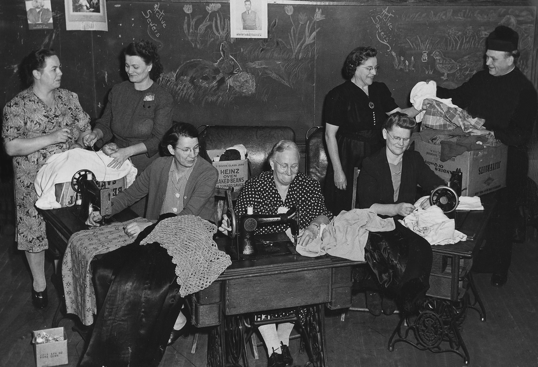 Several women, sitting and standing around sewing machines