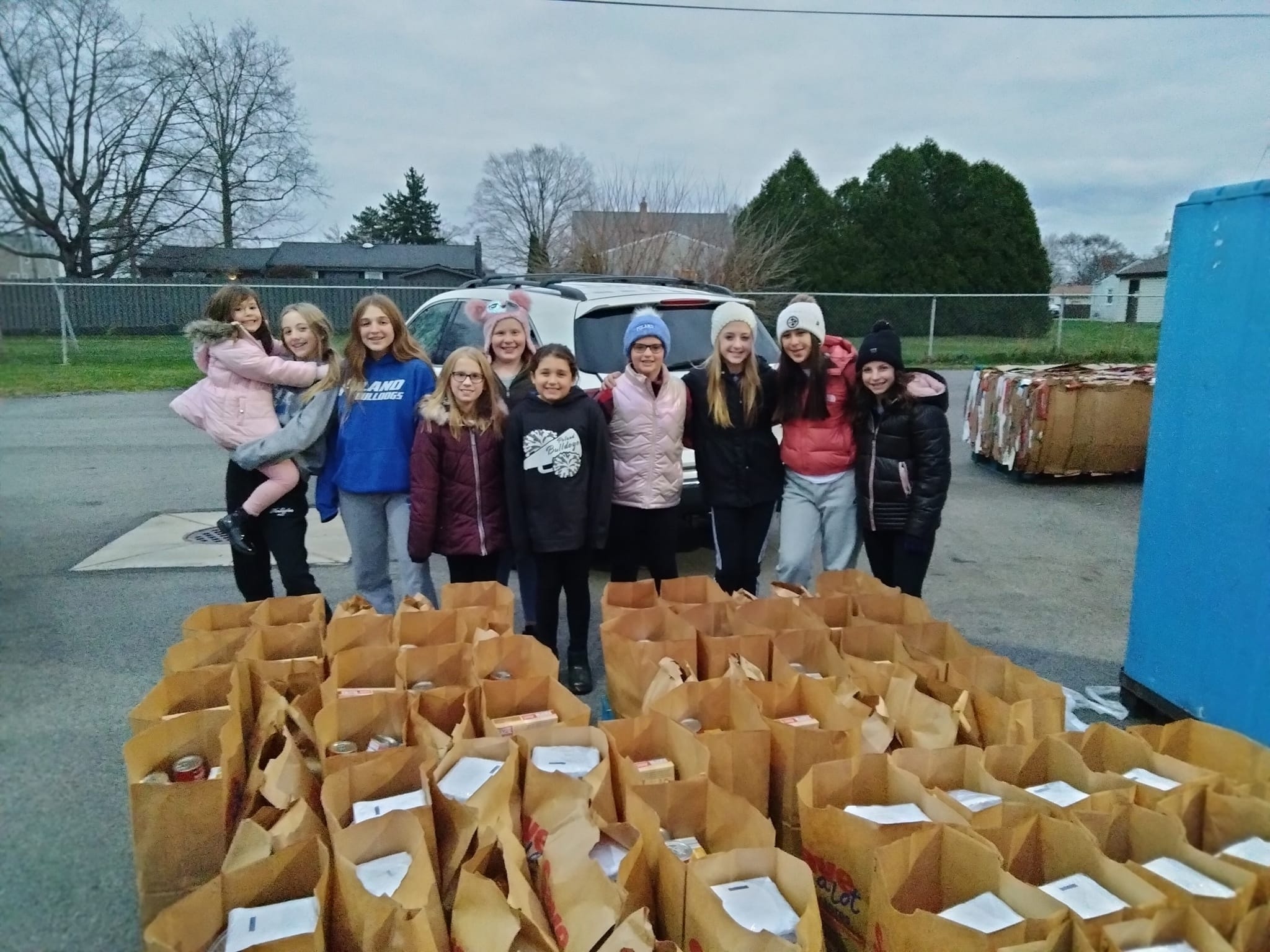 A group of young girls stand around dozens of paper bag donations