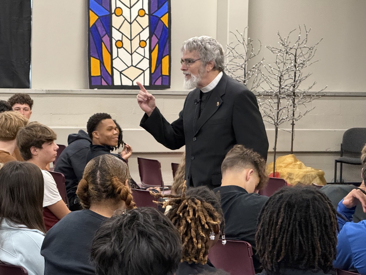 Man in a collar addresses a crowd of students.