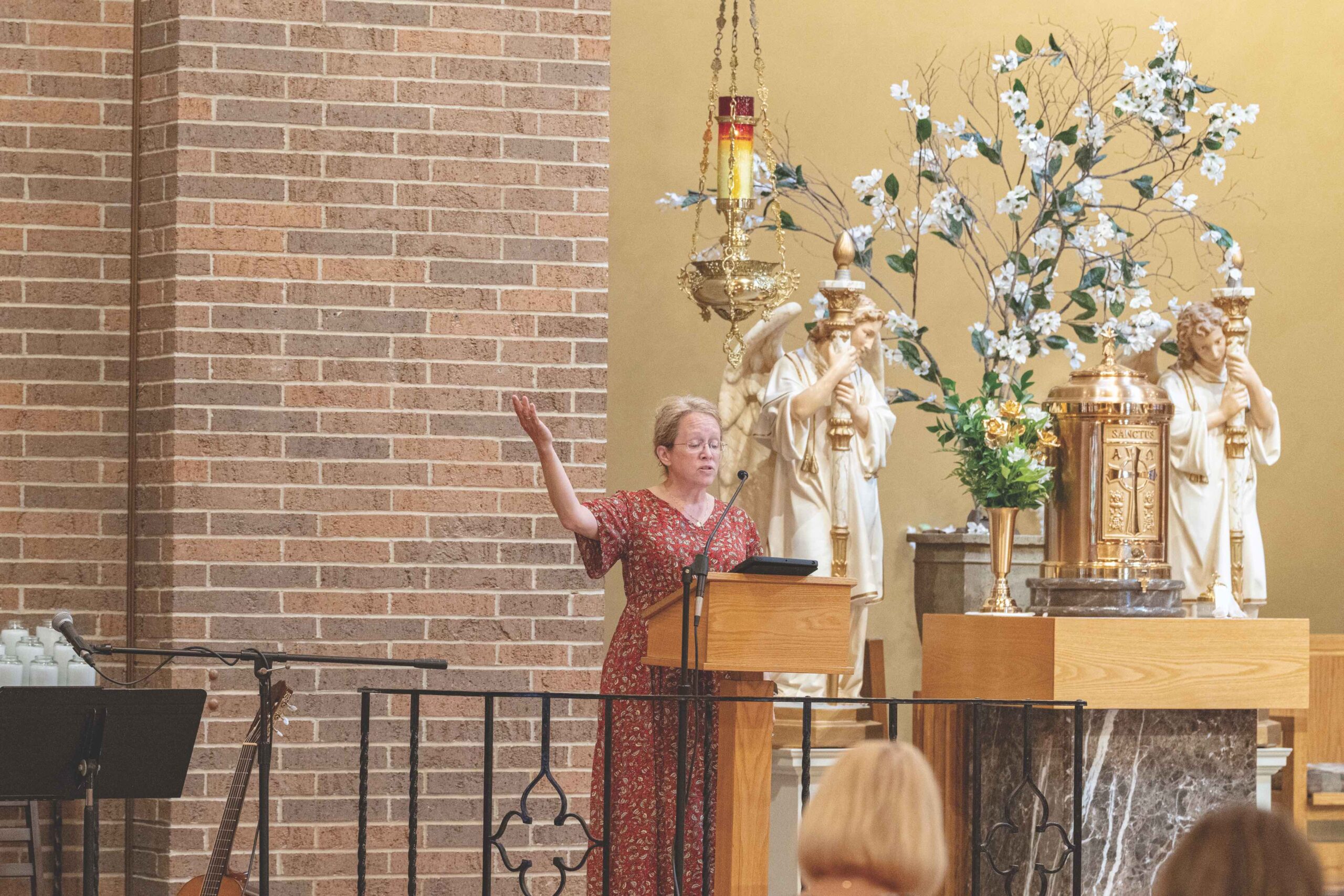 Woman in red dress stands at ambo, with arm raised