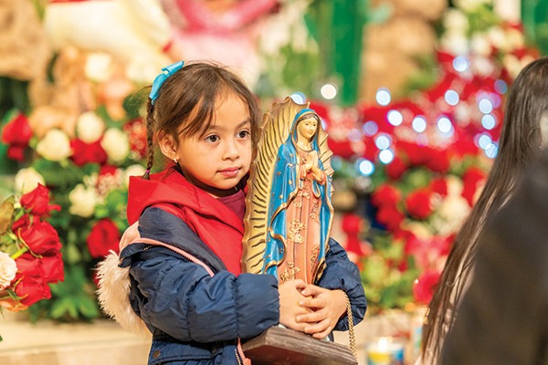 Young child clutches an Our Lady of Guadalupe Statue