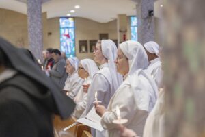 Several oblate sisters stand, holding candles, in white habits at St. Columba Cathedral