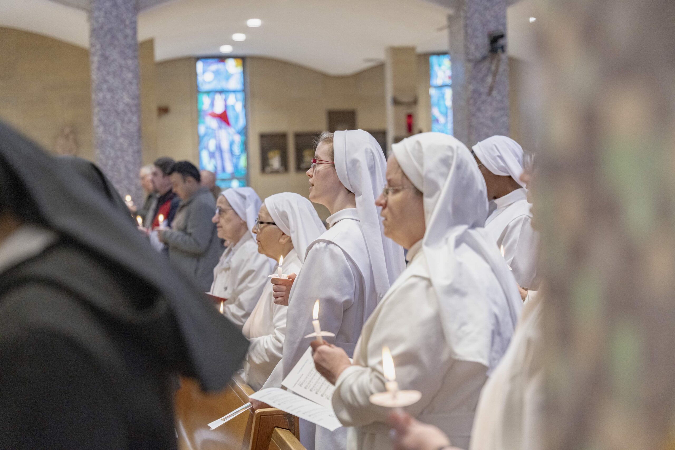 Several oblate sisters stand, holding candles, in white habits at St. Columba Cathedral