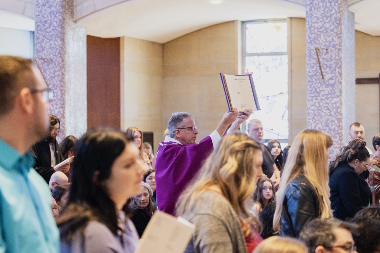 Deacon holds a book aloft during Rite of Election. Photo by Brian Keith.