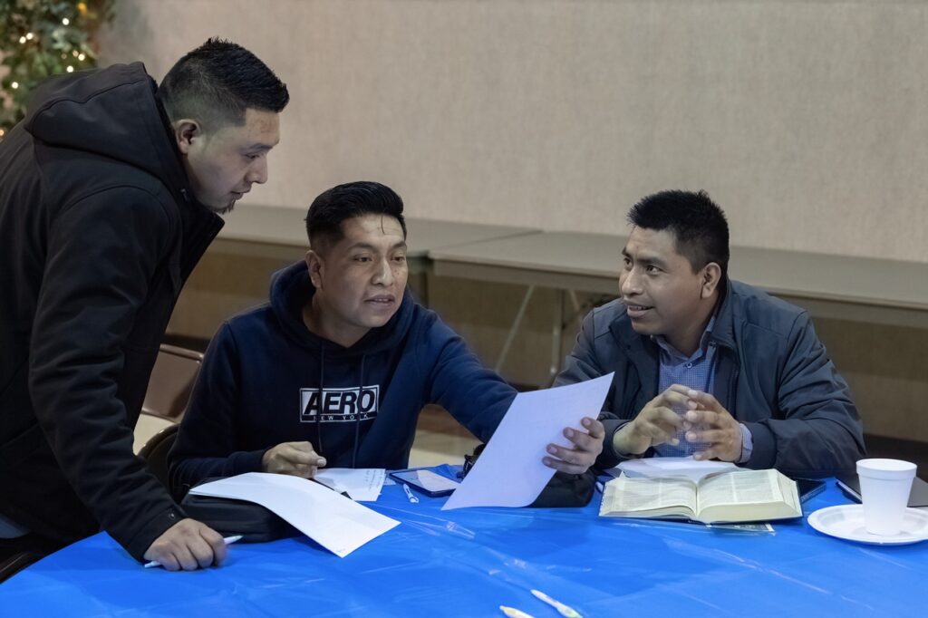 Three men huddle around some papers, discussing, at the hispanic conference 2025. Photo by Bob Rossiter
