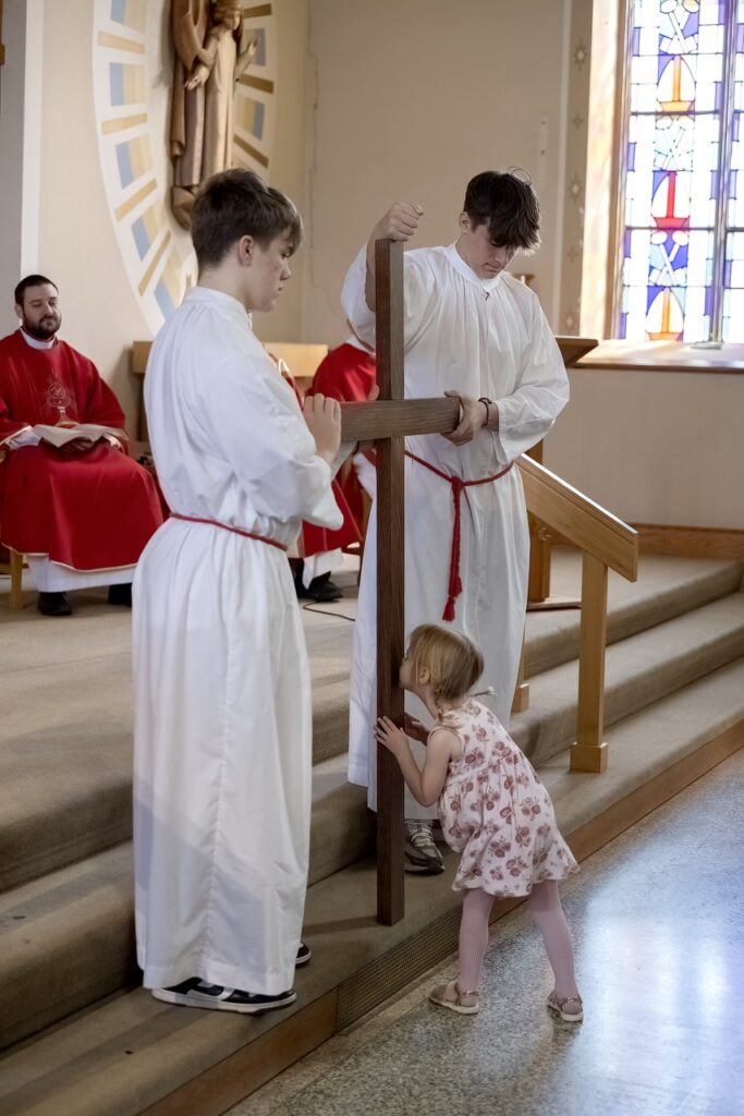 Young girl kisses the cross at Holy Family in Navarre on Good Friday. Photo by Bob Rossiter.