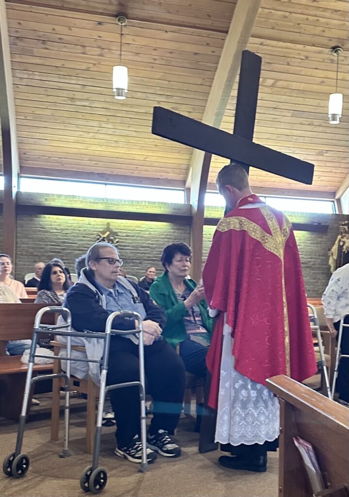 Father brings the cross to the front row of people at Our Lady of Peace Parish in Ashtabula during Good Friday. Photo by Marilou McClimans.