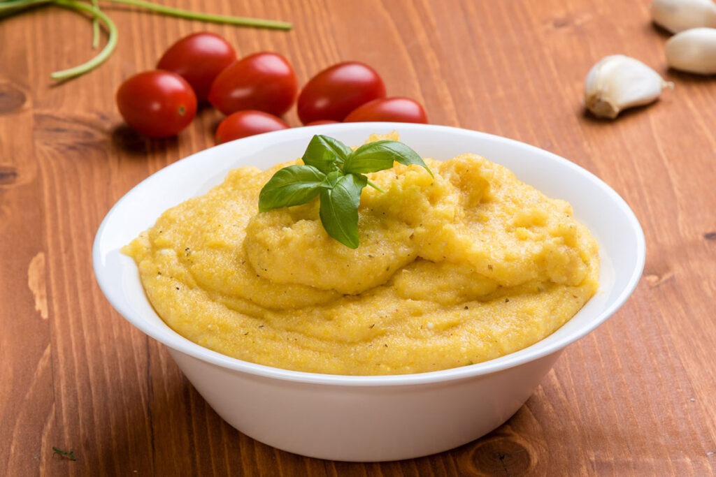 This photo is of a bowl of polenta with tomatoes and a sprig of basil.