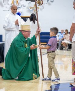 Bishop Bonnar accepts the gifts off a young child at the Mass at St. John School's ribbon cutting