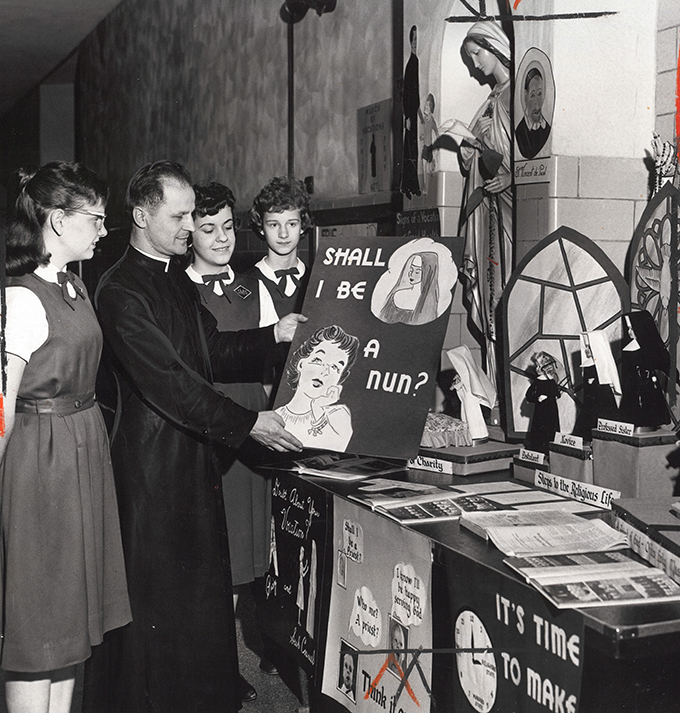 Father Francis Snock assistant pastor of then St. Matthias Parish views vocation posters offered by the 9th Graders of the parishes Junior High School.