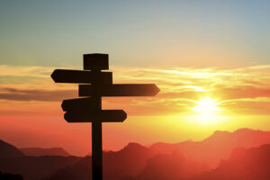 Silhouette of a sign with four directions with mountains and sunset in the background.